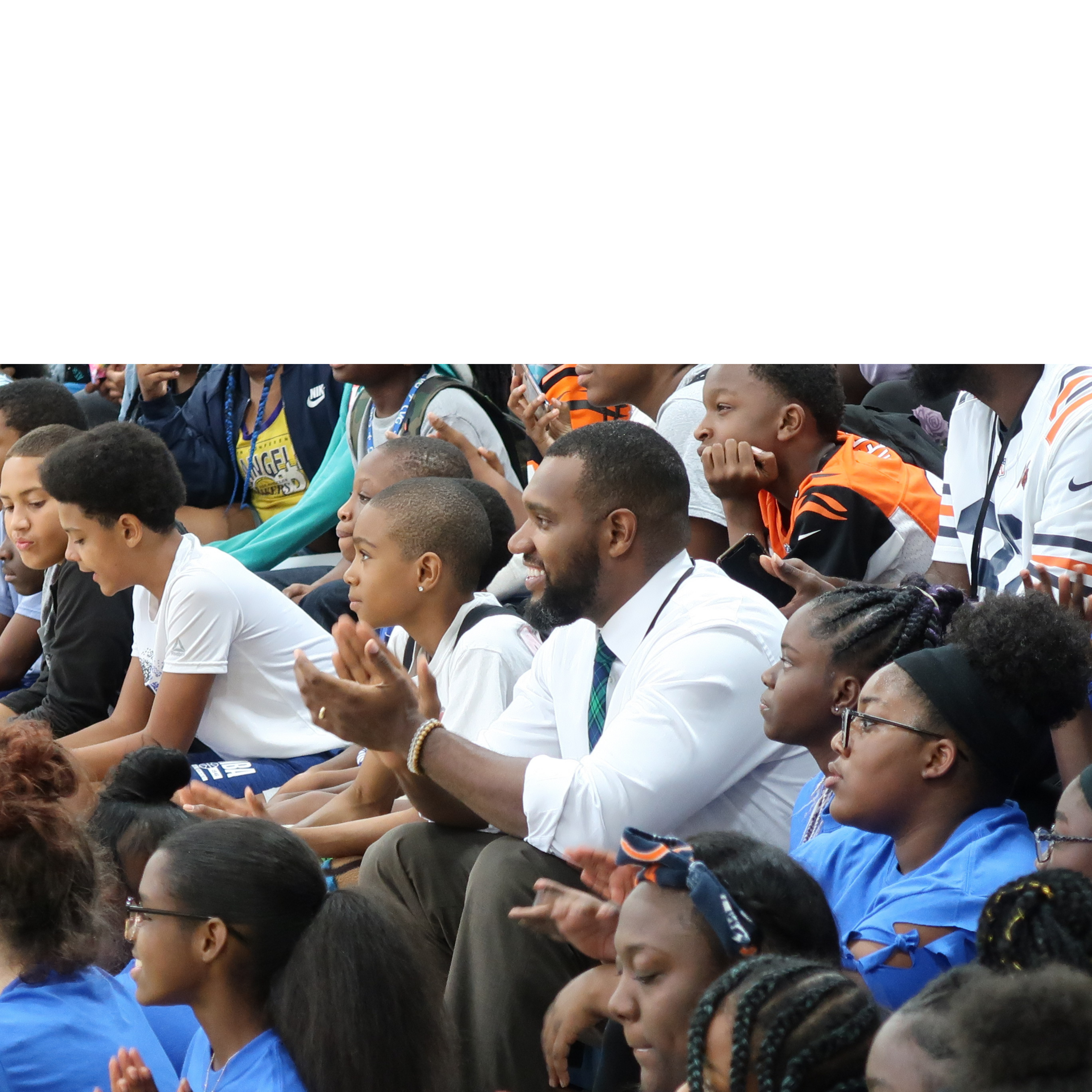 Principal Taylor Porter clapping and smiling surrounded by students sitting on bleachers around him.