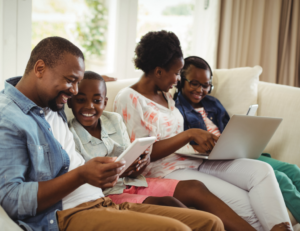 A mom, dad, and two children looking at a laptop and tablet.