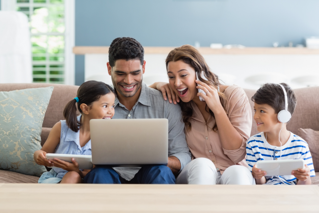 A smiling family with a mom, dad, a son and a daughter smiling and while looking at a laptop screen.