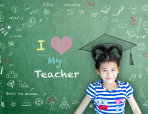 A grade school student A grade school student wearing a graduation cap, next to a chalkboard that says "I heart my teacher."