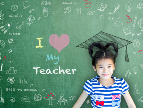 A grade school student A grade school student wearing a graduation cap, next to a chalkboard that says "I heart my teacher."