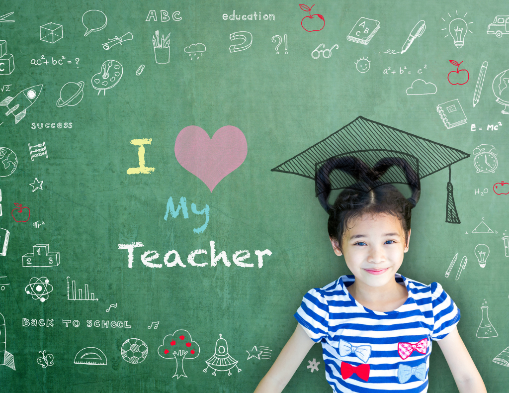 A grade school student A grade school student wearing a graduation cap, next to a chalkboard that says "I heart my teacher."