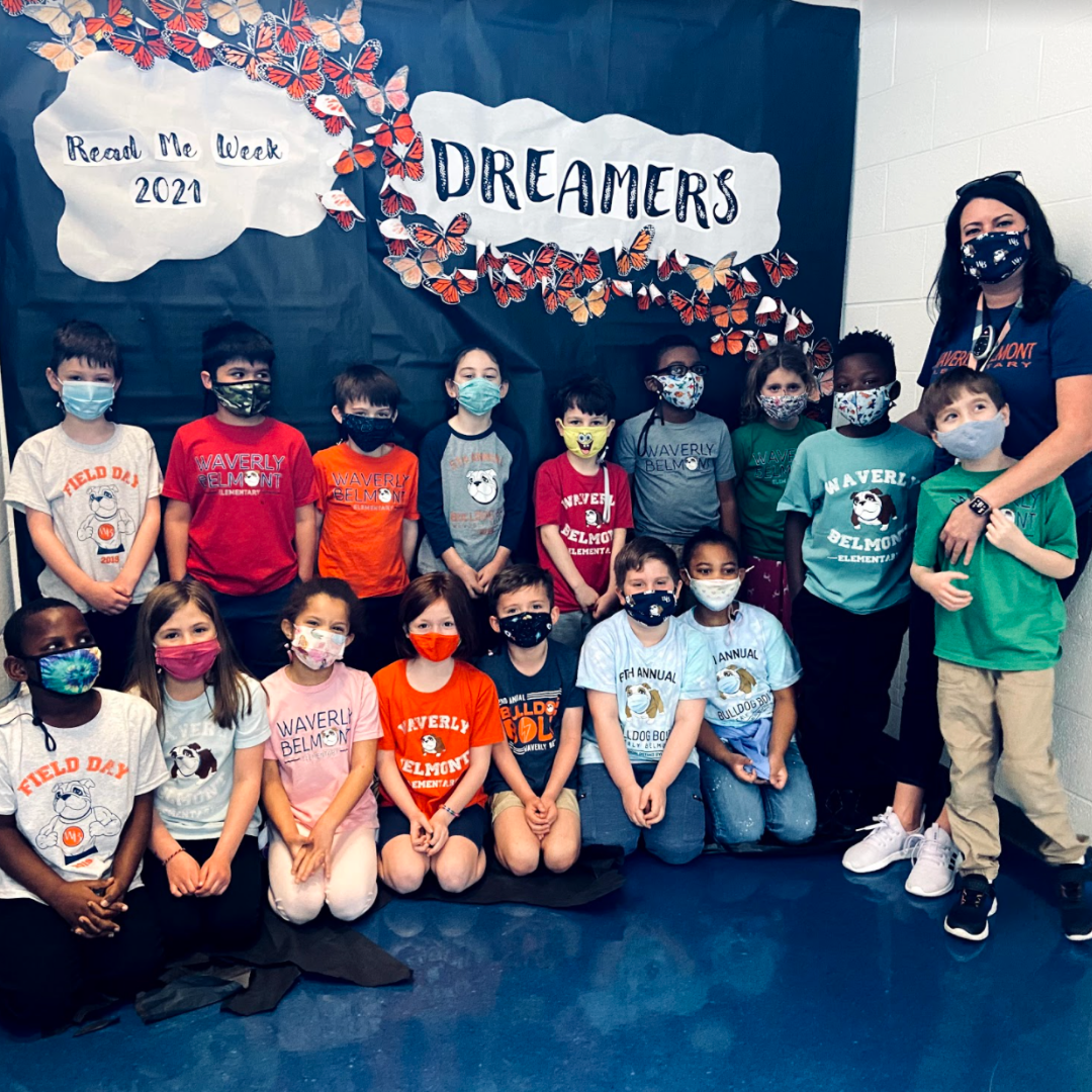 1st grade Teacher Codi Cummings and a group of students in masks in front of a wall that says "Dreamers" and "Read Me Week 2021."