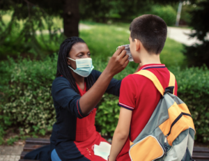 A teacher holding a mask up to a student's face.